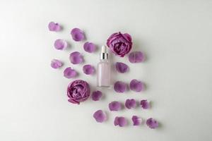 een gezicht serum of essentieel olie in een roze druppelaar fles aan het liegen Aan een wit achtergrond met roos bloemblaadjes in de omgeving van het foto
