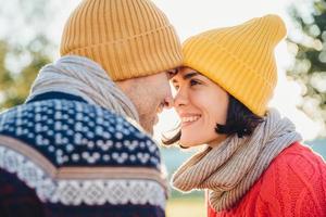 schattige brunette vrouw en haar vriend staan dicht bij elkaar, kijken naar de ogen, glimlachen gelukkig terwijl ze liefde en steun voelen. knappe vrouw met sjaal en hoed heeft date met jonge aantrekkelijke man foto