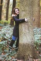jong vrouw knuffelen een boom in Woud- natuur minnaar en boom knuffelaar foto