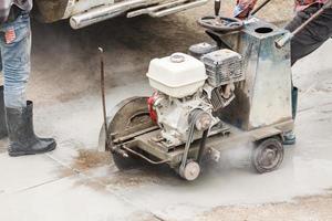 arbeider gebruik makend van diamant zag blad machine snijdend beton weg Bij bouw plaats foto