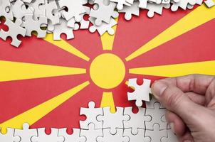 Macedonië vlag is afgebeeld Aan een tafel Aan welke de menselijk hand- vouwen een puzzel van wit kleur foto