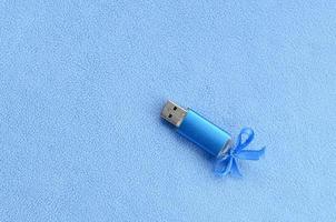 briljant blauw USB flash geheugen kaart met een blauw boog leugens Aan een deken van zacht en harig licht blauw fleece kleding stof. klassiek vrouw geschenk ontwerp voor een geheugen kaart foto