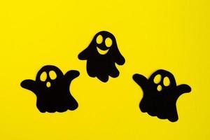 vakantie decoraties voor halloween. drie zwart papier geesten Aan een geel achtergrond, top visie. foto