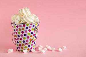 klein kleurrijk emmer gevulde met wit schuimgebak en marshmallows Aan een roze pastel achtergrond. minimaal concept met kopiëren ruimte. foto