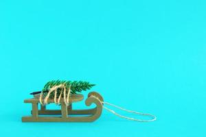 groen houten slee met gebonden kunstmatig Spar boom Aan een helder blauw achtergrond. Kerstmis en nieuw jaar concept met kopiëren ruimte. foto