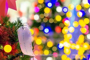 papier hangende Aan Kerstmis boom voor vakantie decoratie met kleurrijk lichten Aan achtergrond. foto