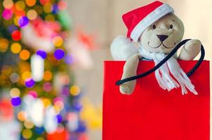 de kerstman teddy beer in boodschappen doen zak met wazig focus van kleurrijk Kerstmis boom voor vakantie decoratie achtergrond. foto