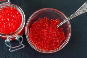 rood kaviaar in glas pot met zilver lepel . zee voedsel. gezond aan het eten. eetpatroon. zwart achtergrond. foto