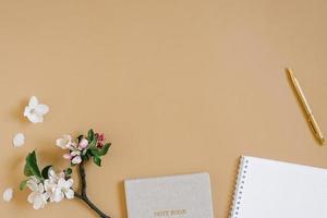 vlak leggen e in beige tonen voor een eigen baas freelance meisje. planner, pen en wit bloemen van appel boom. vaag notitieboekje of notitieboekje model. foto