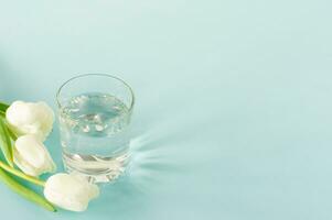 een glas van zuiver water met tulpen Aan blauw achtergrond. kopiëren ruimte voor tekst. consept van Gezondheid leven en eetpatroon foto