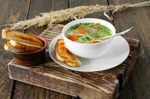 traditioneel kip soep met noedels ans wortels geserveerd in een kom over- houten achtergrond foto