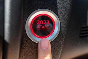 vinger druk op een auto-ontstekingsknop met 2023 starttekst in de auto. nieuwjaar nieuwe jij, voorspelling, resolutie, motivatie, verandering, doel, visie, innovatie en planningsconcept foto