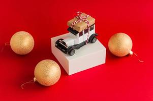 kinderen speelgoed- auto Aan een wit truc met een geschenk Aan de dak Aan een rood achtergrond met gouden Kerstmis ballen. foto