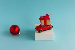 rood speelgoed- auto met een nieuw jaar geschenk Aan de dak Aan een wit pouill en een blauw achtergrond. de concept van nieuw jaar kortingen en verkoop. foto