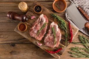 top visie van een houten tafel met gebarbecued varkensvlees steaks van boer vlees. specerijen voor Koken Aan een houten bord. foto