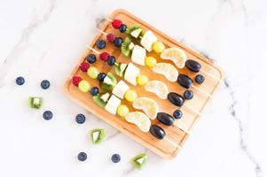 fruit canapeetjes Aan een houten bord.heerlijk en gezond voedsel.mix van mandarijn, kiwi, banaan, druiven.view van bovenstaande. foto