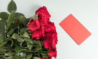 een groot boeket van mooi rood rozen Aan een wit achtergrond met een ansichtkaart voor schrijven uw tekst. feestelijk samenstelling. foto