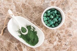 poeder en spirulina tablets in kommen Aan een marmeren tafel. top visie. superfood, dieet supplement. bron van vitamine eiwit en beta-caroteen. foto