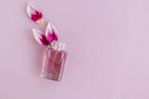 een transparant fles van parfum of toilet bowling water Aan een Purper achtergrond met tulp bloemblaadjes. top visie. een kopiëren van de ruimte. foto
