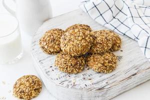 havermout eigengemaakt koekjes met sesam en vlas zaden Aan een wit houten bord detailopname. een glas van melk, een linnen servet. foto