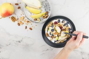 de hand- van een jong vrouw met een lepel van muesli gevulde gedurende ontbijt. bord met muesli, bessen, rijp Peer. blended voedsel, fitheid, eetpatroon. foto