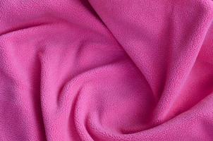 de deken van harig roze fleece kleding stof. een achtergrond van licht roze zacht pluche fleece materiaal met een veel van Verlichting vouwen foto