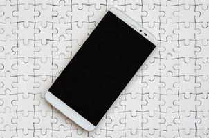 een modern groot smartphone met een tintje scherm leugens Aan een wit decoupeerzaag puzzel in een gemonteerd staat foto