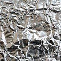 dun gerimpeld vel van verpletterd blik aluminium zilver folie achtergrond met glimmend verfrommeld oppervlakte voor structuur foto