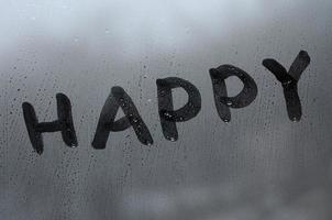 de Engels woord gelukkig is geschreven met een vinger Aan de oppervlakte van de beneveld glas foto