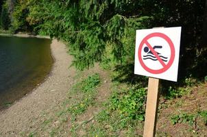 een pijler met een teken aanduiding een verbod Aan zwemmen. de teken shows een doorgestreept drijvend persoon foto