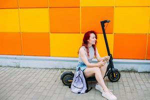 vrouw gebruikt een smartphone en een elektrische scooter in de zomer in de stad foto