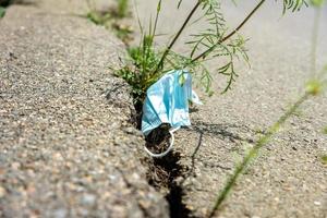 gebruikt medisch masker en planten in een barst Aan de stoep. ecologisch concept over de gevolg van de pandemisch Aan de toenemen in de bedrag van vuilnis foto