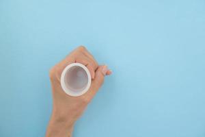 detailopname van een vrouw hand- Holding een menstruatie- kop tegen een blauw achtergrond. vrouwen Gezondheid concept, nul verspilling alternatieven. foto