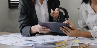 detailopname van handen gebruik makend van digitaal tablet, twee bedrijf collega vergadering naar bespreken de nieuw project bedrijf strategie plan Aan houten tafel in kantoor. briefing, brainstormen, overleg plegen. foto