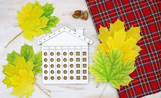 geel bladeren, rood geruit plaid, eikels en gesneden houten huis. concept van verkoop echt landgoed, herfst, huren foto