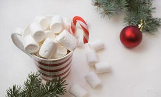 heet chocola met marshmallows in een rood en wit bakkerij Aan een wit achtergrond en takken van een nieuw jaar boom. foto