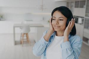 gelukkig vrouw in hoofdtelefoons luister naar muziek, podcast of audio boek genieten van perfect geluid Bij huis foto