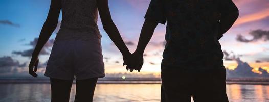 achterzijde visie van volwassen toerist Aziatisch liefde paar Holding hand- Aan de strand met zonsondergang lucht achtergrond foto