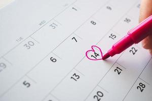 vrouw hand- met pen Mark hart vorm Aan kalender datum Bij 14e Valentijn dag foto
