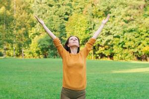 schattig vrouw staand in voorjaar natuur park met breed Open armen verheven omhoog foto
