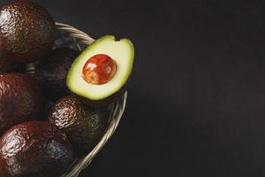 rijp hass avocado en een ontpit plak in een mand Aan een zwart getextureerde achtergrond. foto