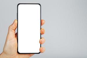 hand- houdt zwart smartphone met blanco wit scherm en modern frameloos ontwerp geïsoleerd Aan grijs achtergrond. foto