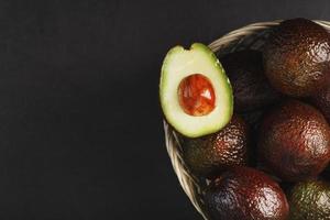 rijp hass avocado en een ontpit plak in een mand Aan een zwart getextureerde achtergrond. foto