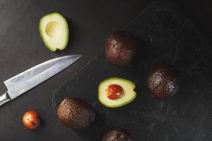 gesneden en geheel biologisch avocado hass met een mes Aan een zwart achtergrond. foto