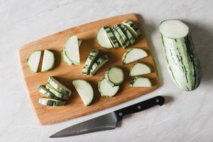 courgette besnoeiing in plakjes Aan snijdend bord, voor de helft squash, mes Aan wit tafel, overhead visie foto