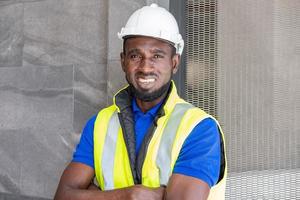 selectief focus Bij gezicht van zwart Afrikaanse voorman Bij gebouw bouw plaats, vervelend beschermend hoed en veiligheid apparatuur, glimlach en gevoel gelukkig Bij werk. civiel ingenieur werken. foto