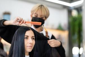 Kaukasisch Dames met haar- elegant terwijl Doen haar- besnoeiing en vervelend chirurgisch gezicht masker terwijl styling haar- voor cliënt. professioneel bezigheid, schoonheid en mode onderhoud nieuw normaal foto