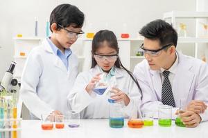 jong Aziatisch jongen en meisje glimlach en hebben pret terwijl aan het doen wetenschap experiment in laboratorium klas met docent. studie met wetenschappelijk uitrusting en buizen. onderwijs concept. foto