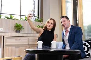 selectief focus Bij smartphone. jong Kaukasisch paar dating binnen van de koffie winkel terwijl Dames nemen selfie foto van mobiel telefoon. dating werkzaamheid, modern verhouding levensstijl concept.