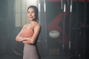 selectief focus Bij Aziatisch Dames vervelend sport kleding met glimlach binnen van de Sportschool voordat oefening en gewicht hijs- binnen geschiktheid Sportschool naar training voor fysiek lichaam sterkte en firma armen spier foto